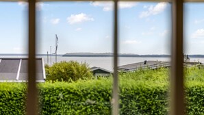 A view through a window of a building with a rooftop garden, a solar panel, and a distant shoreline.