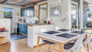 A modern kitchen with blue cabinets, a central island, and a dining area with a white table and chairs.