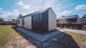 A modern, single-story building with a sloped roof, large windows, and a paved entrance area. - Spacious Nature Retreat (Bant)