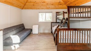 A room with a wooden ceiling, a gray sofa, a bunk bed, and a window. - Wasaga Beach Summer Cottages & Cabins (Wasaga Beach)