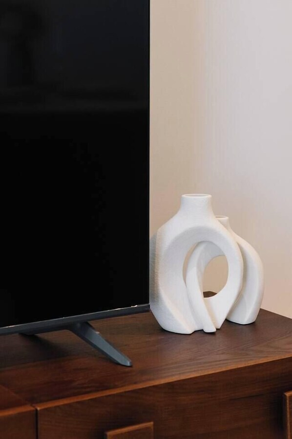 Un televisor de pantalla plana sobre un mueble de madera con dos jarrones blancos y abstractos a su lado.