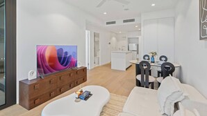 A modern living room with a flat-screen TV, a wooden cabinet, a dining area with a table and chairs, and a kitchen in the background. - Stylish 1-Bedroom Near Casino Luxe Tower Street & South Bank (Brisbane City)