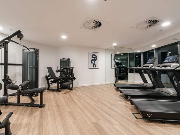 A gym with treadmills, weight machines, and a mirror wall.