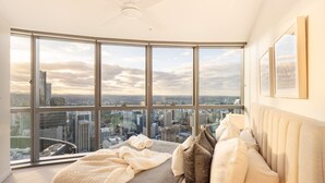 A bedroom with a large window offering a city view, a ceiling fan, and a bed with pillows and a blanket.