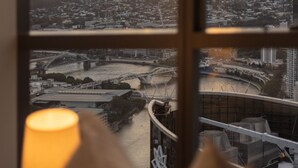 A view through a window of a cityscape at sunset with mountains in the background and a bridge in the foreground.