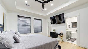 A modern bedroom with a large bed, a desk, and a TV mounted on the wall. - 6BR Funhouse w/ Court, Pool Table Dining & TV in Every Bedroom (Houston)