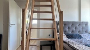 Eine Holztreppe im Loft-Stil in einem Schlafzimmer mit einer gepolsterten Kopfstütze und einem Bett mit himmelblau-weißer Bettdecke.
