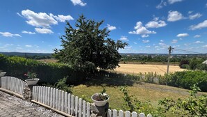 Ein Garten mit weißem Zierzaun, einem großen Baum und einem Feld im Hintergrund.