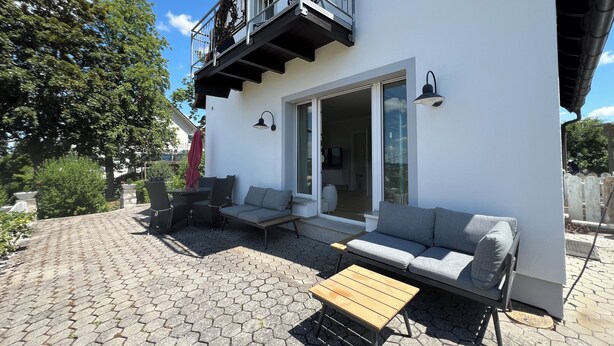 Eine moderne Außenpatio mit einem sechseckigen Fliesenboden, einem Holztisch, einem grauen Sofa und einem Balkon mit Metallgeländern.