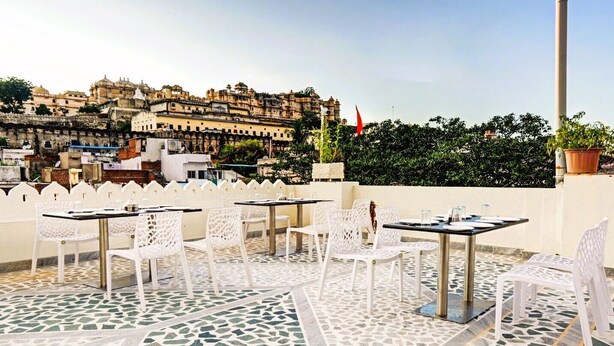 Une terrasse extérieure avec des chaises et des tables blanches, un sol à motifs et une vue sur un bâtiment historique en arrière-plan.