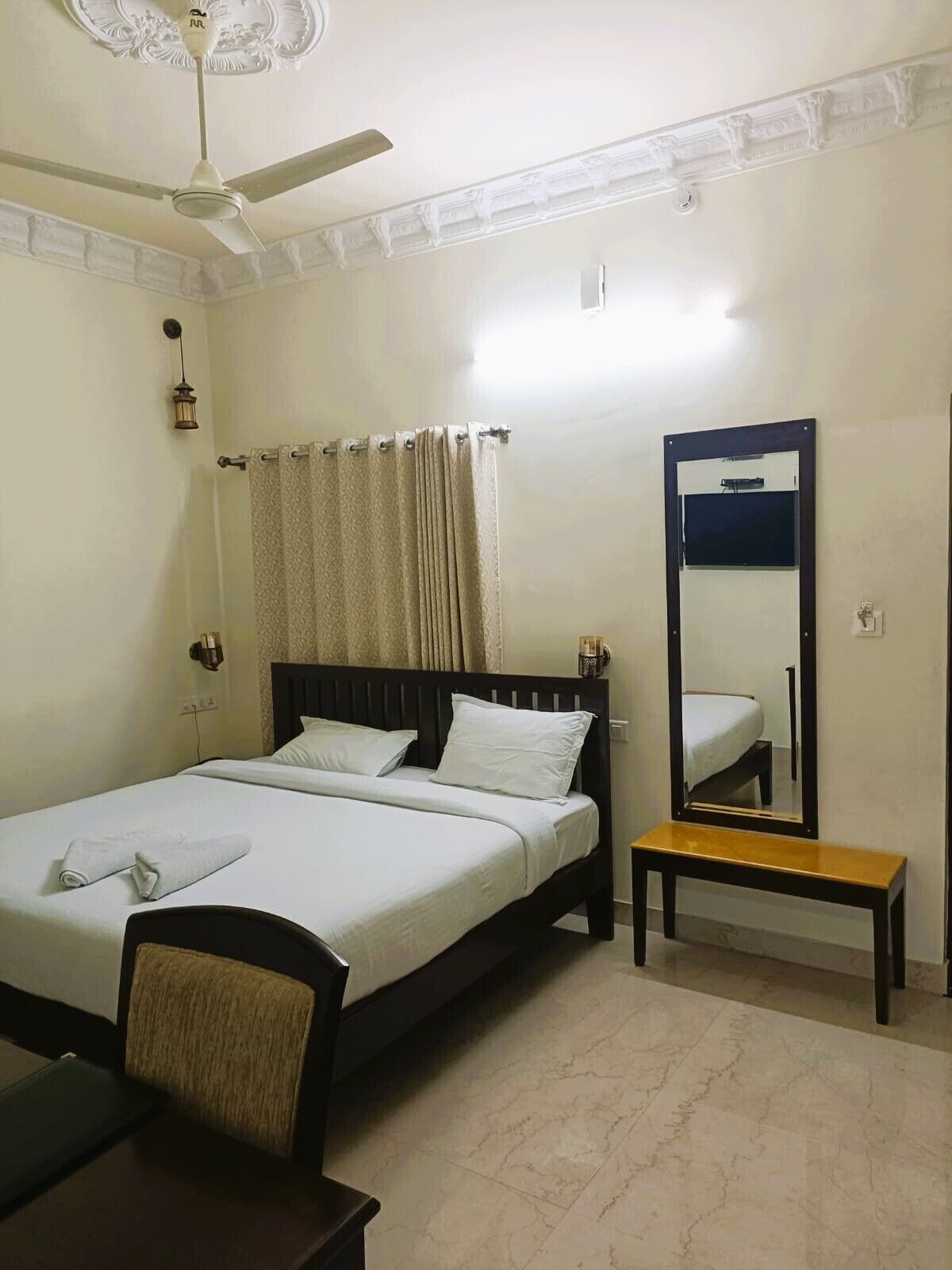 Habitación de hotel con una cama individual, una mesita de noche, una silla, un ventilador de techo y un espejo grande.