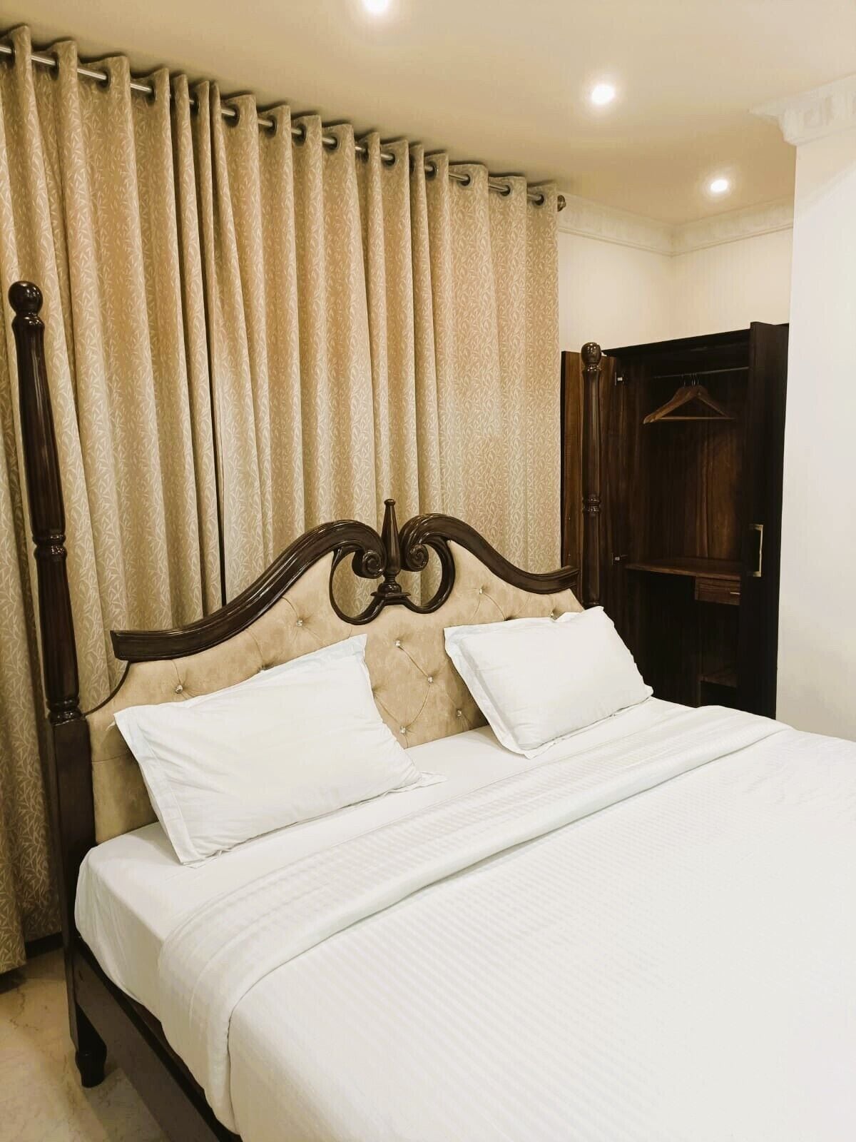 A neatly made bed with a wooden headboard, beige curtains, and a wooden wardrobe.