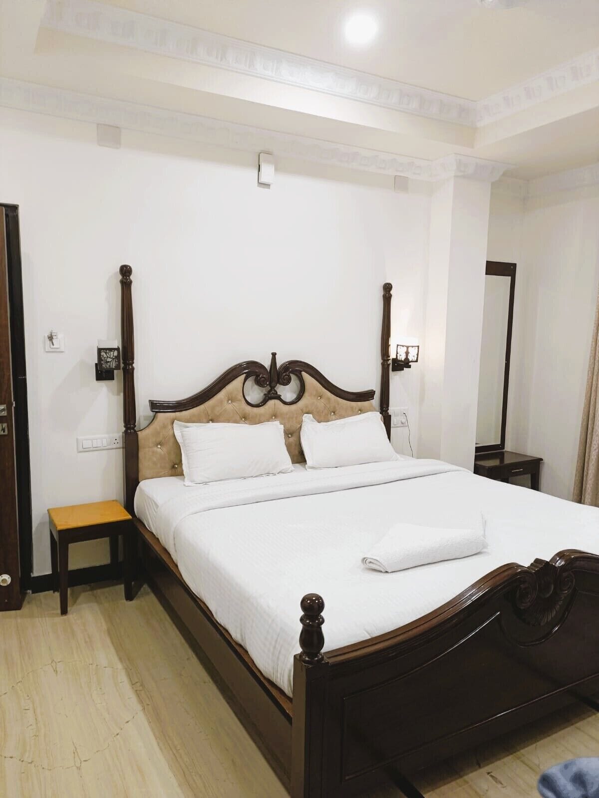 Uma cama bem arrumada com cabeceira de madeira, mesa de cabeceira e criado-mudo com abajur.