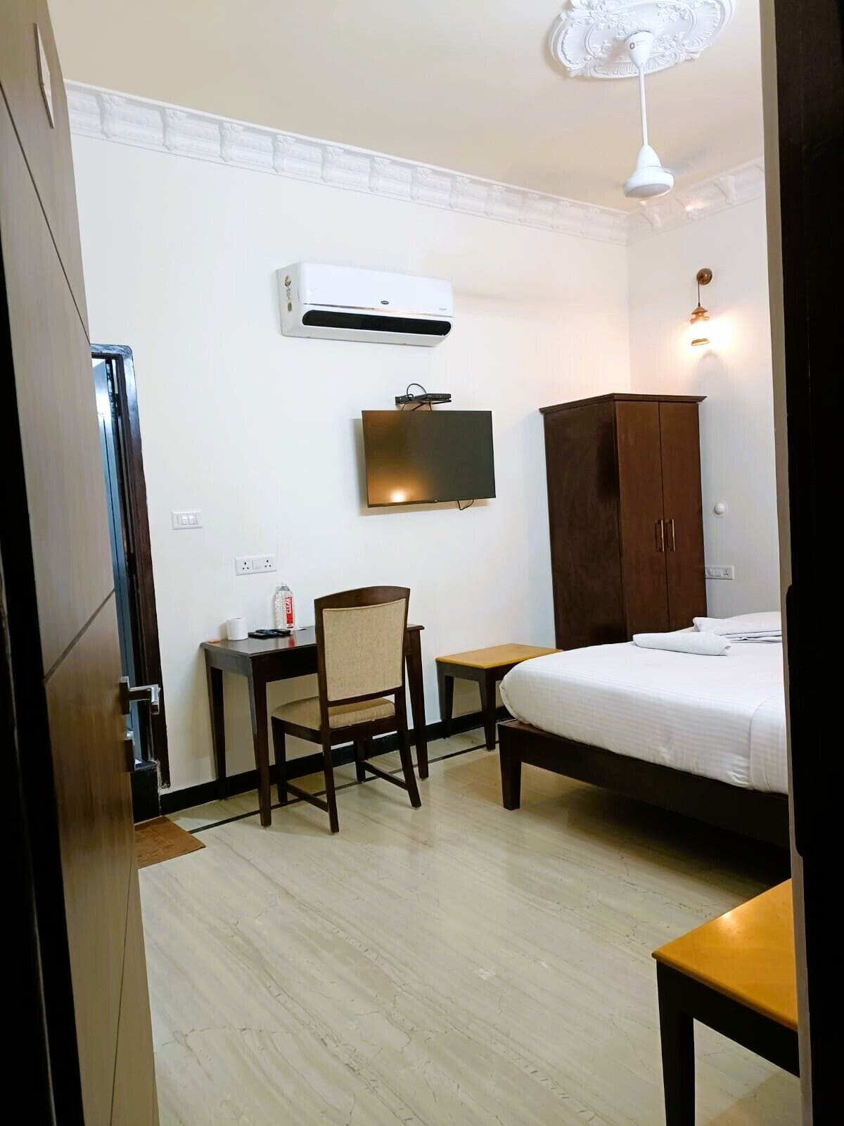 Una camera d'albergo con un letto, una scrivania con una sedia, una televisione, un armadio e un condizionatore d'aria.