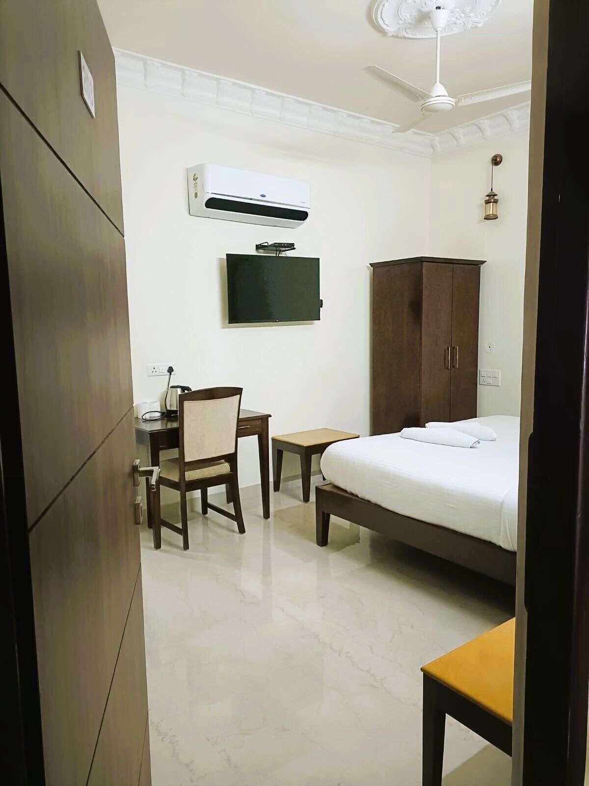 Habitación de hotel con cama, escritorio, silla, armario, televisor y aire acondicionado.