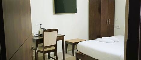 Habitación de hotel con cama, escritorio, silla, armario, televisor y aire acondicionado.