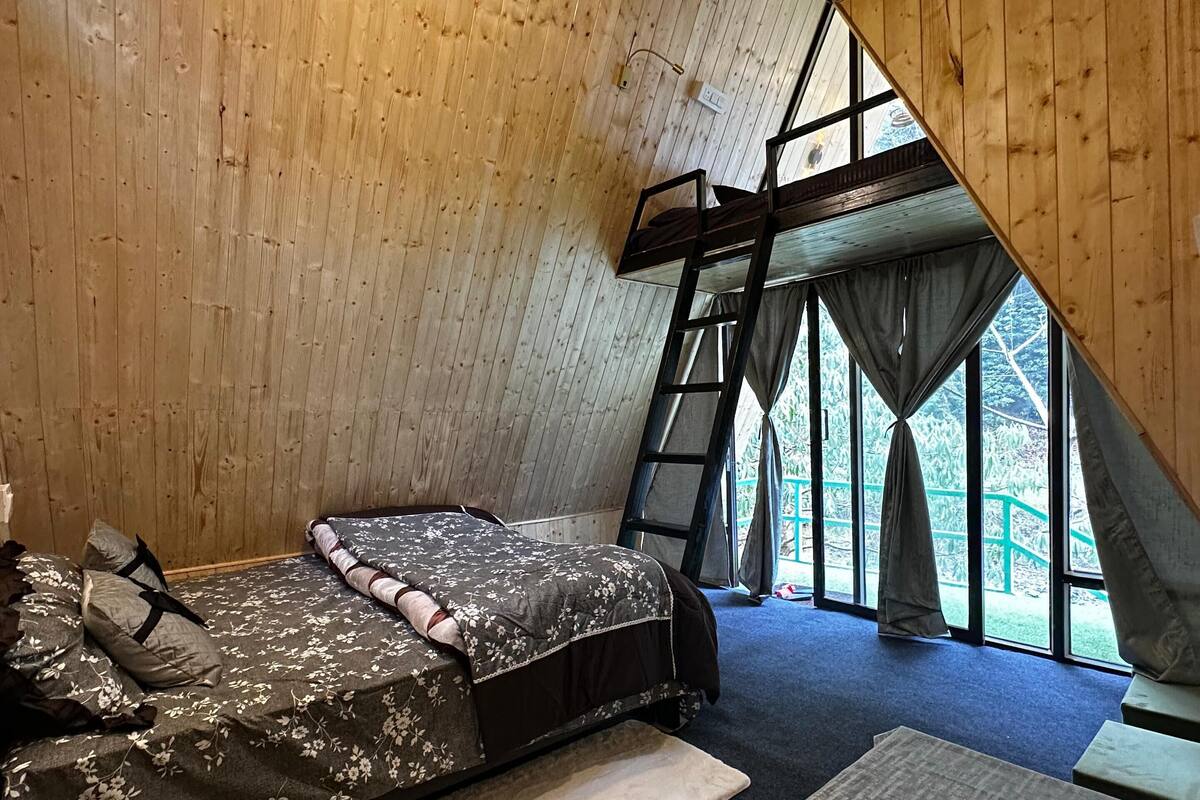 Una cabaña acogedora con cama altillo, una mesita con hervidor y vistas al exterior a través de amplias ventanas.