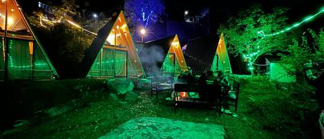 A series of triangular tents with string lights, a fire pit, and a stone bench.
