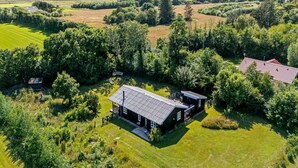 Vue aérienne d’une propriété rurale avec une grande maison entourée de champs et d’arbres.