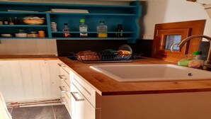 Una cucina con un piano di lavoro in legno, un lavello e un espositore per piatti. Si vedono pensili sotto il piano e uno scaffale blu sopra.