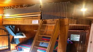 Interno di una baita di legno con un letto a castello, una scala e una finestra.