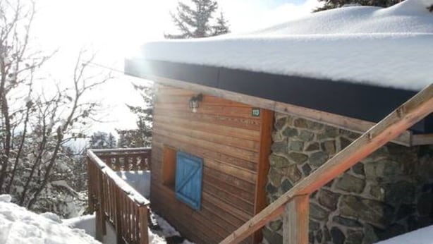 Una baita di legno con parete in pietra, un molo in legno e una porta blu.