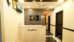 Ein Hotel-Rezeptionsbereich mit einer Marmor-Theke mit der Aufschrift 'Reception', einem Deckenventilator und einem Schild, das 'Hotel Rinza Residency' anzeigt.