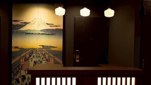 Un mostrador de recepción con diseño tradicional japonés, iluminado por lámparas colgantes, y un mural con el Monte Fuji al fondo.