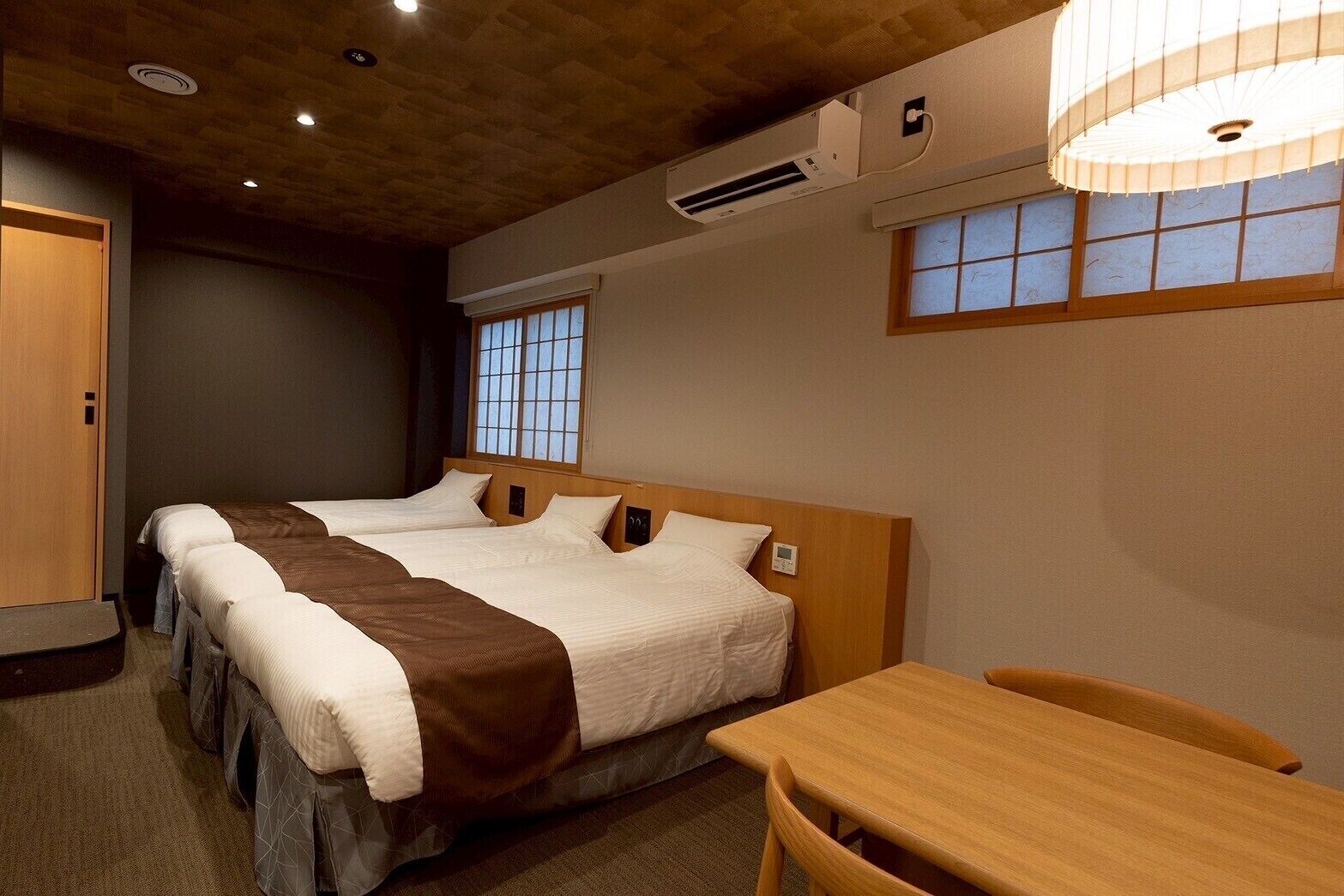 A hotel room with two beds, a wooden table, and a window with a view.