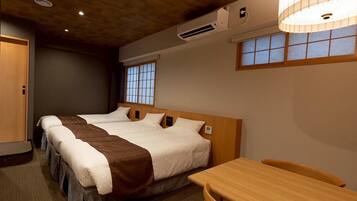 A hotel room with two beds, a wooden table, and a window with a view.