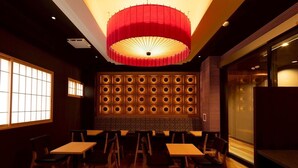 Interior de restaurante con mesas y sillas de madera, lámpara colgante roja y pared con paneles iluminados circulares.