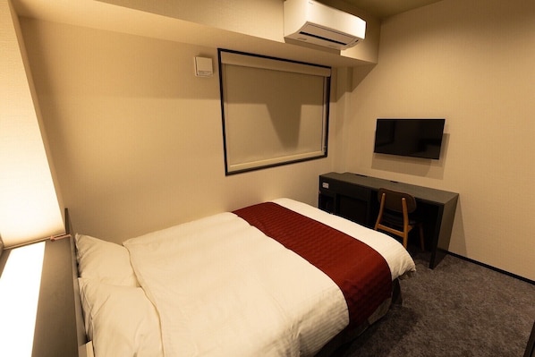 Quarto de hotel com cama, escrivaninha, cadeira, televisão e ar condicionado.