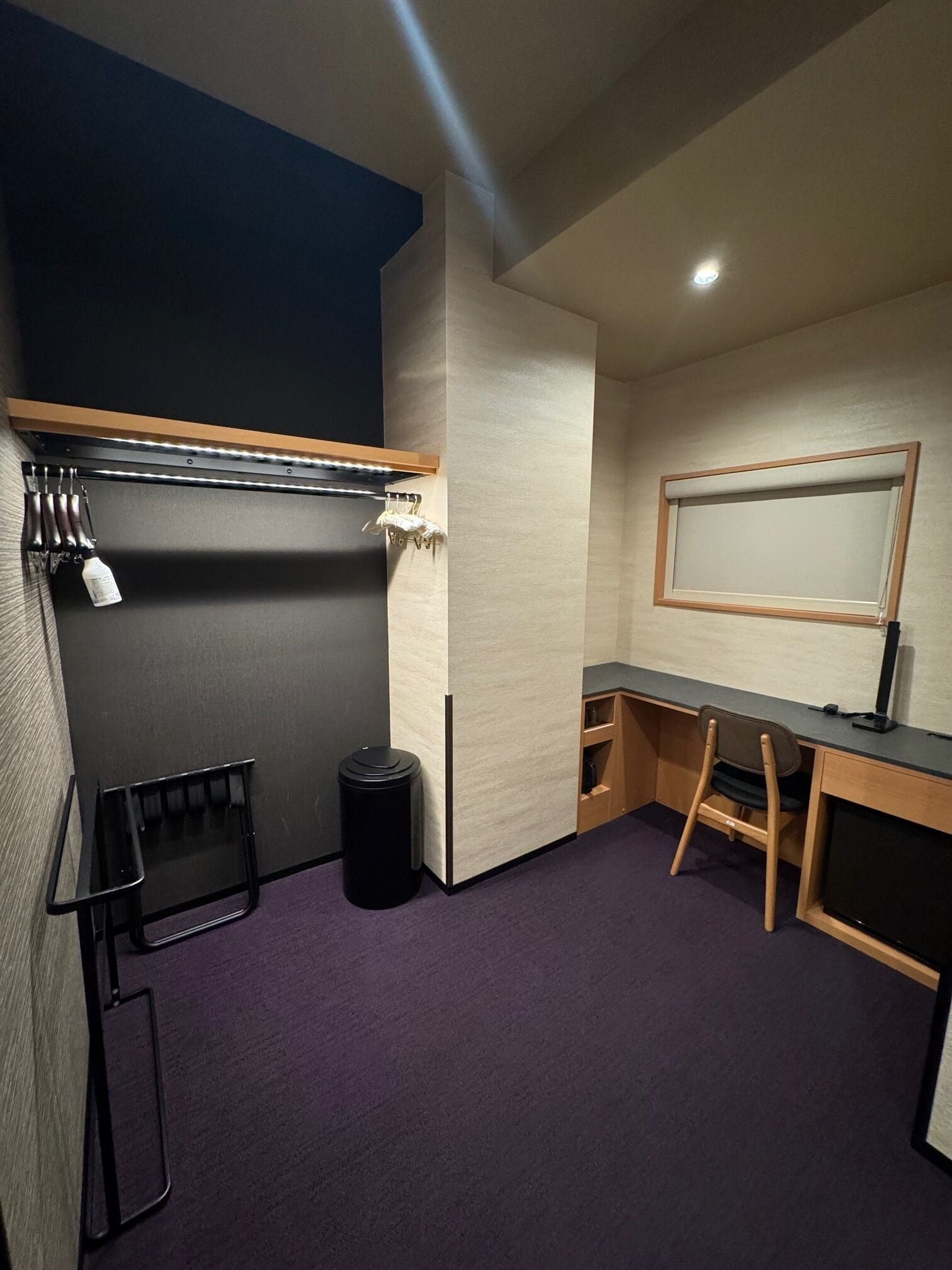 A compact room with a desk, chair, and a small trash bin.