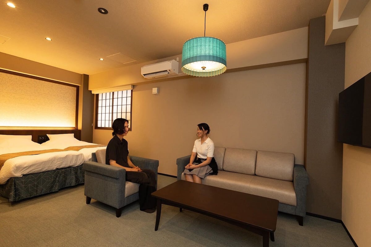 Una habitación de hotel con una cama, dos sillones, un sofá, una mesa de centro y un televisor.