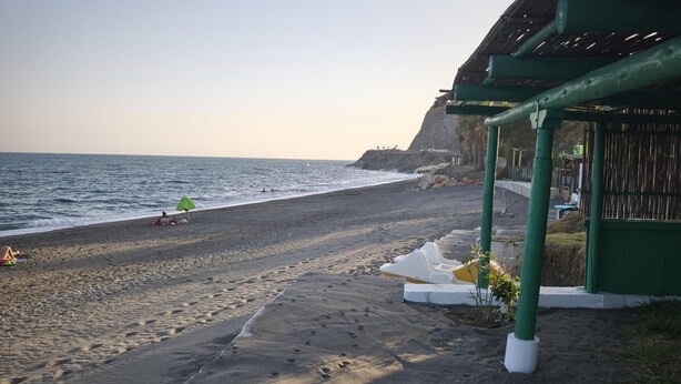 A beach with footprints leading to a sheltered area with a green roof.