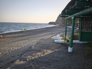 Ein Strand mit Fußspuren, die zu einer geschützten Bucht mit einem begrünten Dach führen.