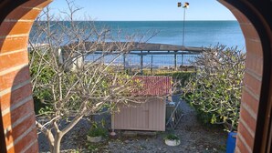 A view through a brick archway of a garden with a wooden deck, a shed, and a fence overlooking the sea.