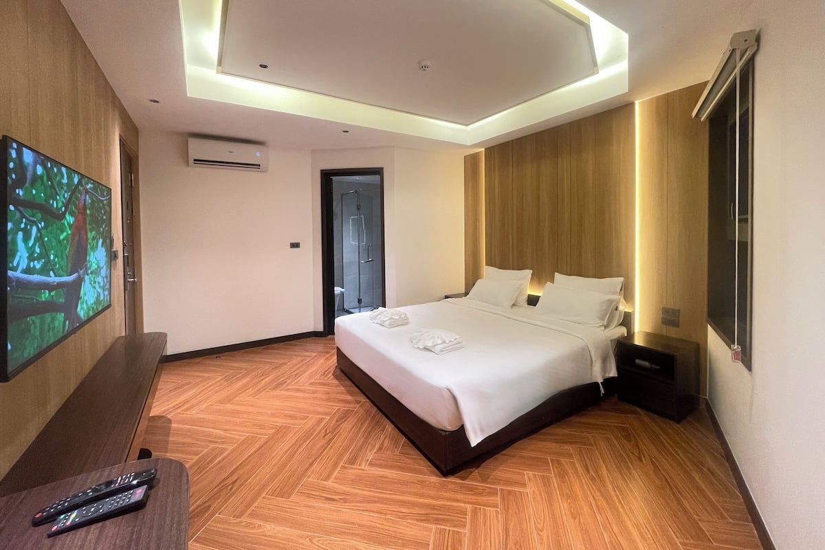 Une chambre d’hôtel moderne avec un grand lit, un téléviseur à écran plat fixé au mur et un plancher en bois.