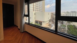 Ein Zimmer mit großem Fenster, Holzboden und Blick auf die umliegenden Gebäude.