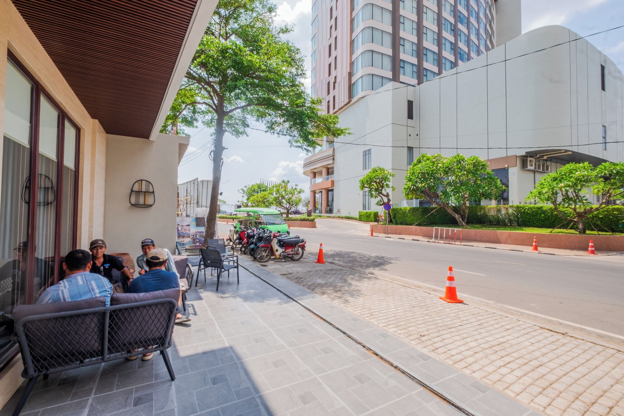 A building with a modern design, a paved sidewalk, and a street with parked motorcycles and traffic cones.