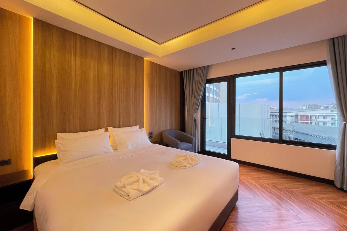 Une chambre d’hôtel avec un grand lit, une chaise et une grande fenêtre donnant sur la ville.