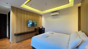 A hotel room with a large bed, a flat-screen TV mounted on the wall, a coffee machine, and an air conditioning unit.