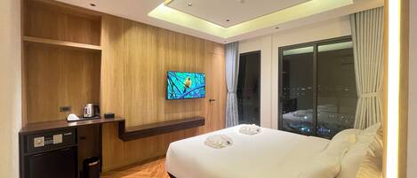 A modern hotel room with a wooden panel wall, a flat-screen TV mounted above a wooden console, a bed with white linens, and a large window offering a city view.
