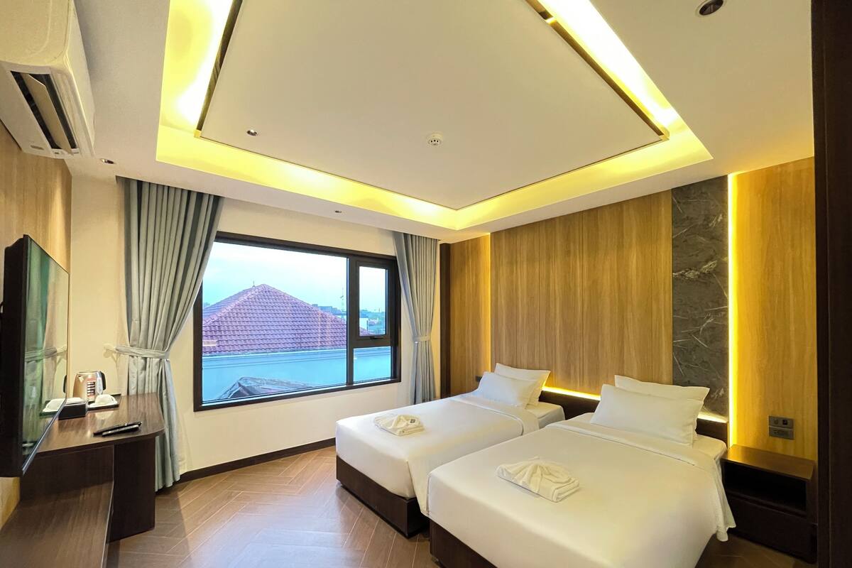 Une chambre d’hôtel avec deux lits, une grande fenêtre donnant sur un immeuble, un téléviseur à écran plat et un plancher en bois.