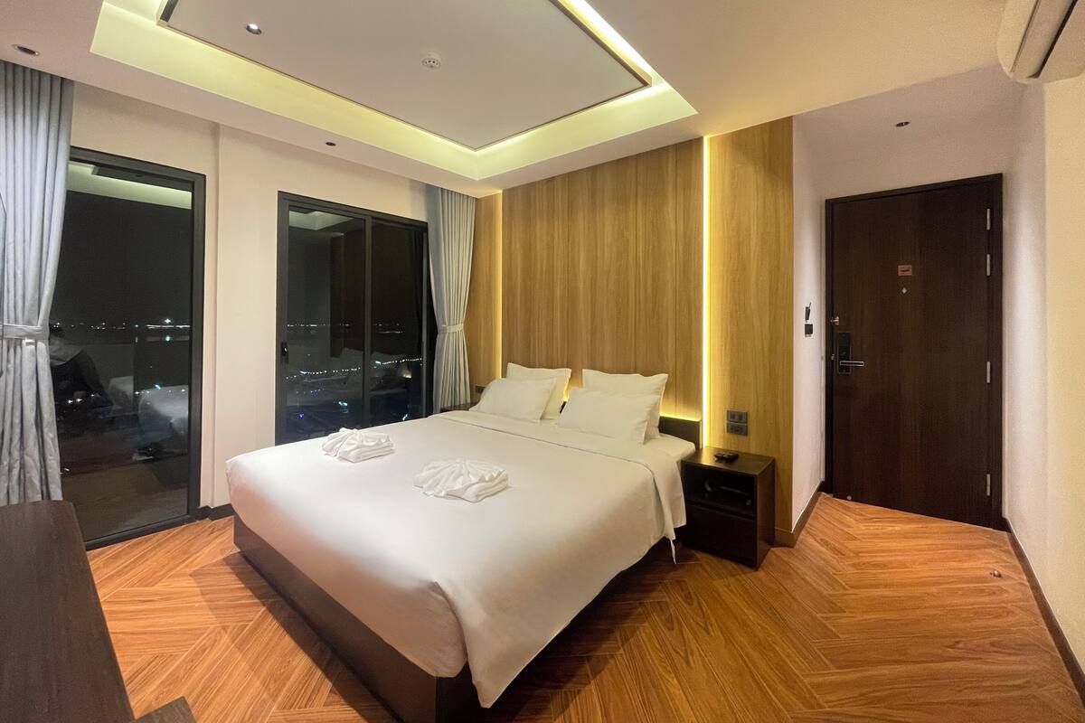 Une chambre d’hôtel moderne avec un grand lit, un plancher en bois, une table de chevet et une porte.