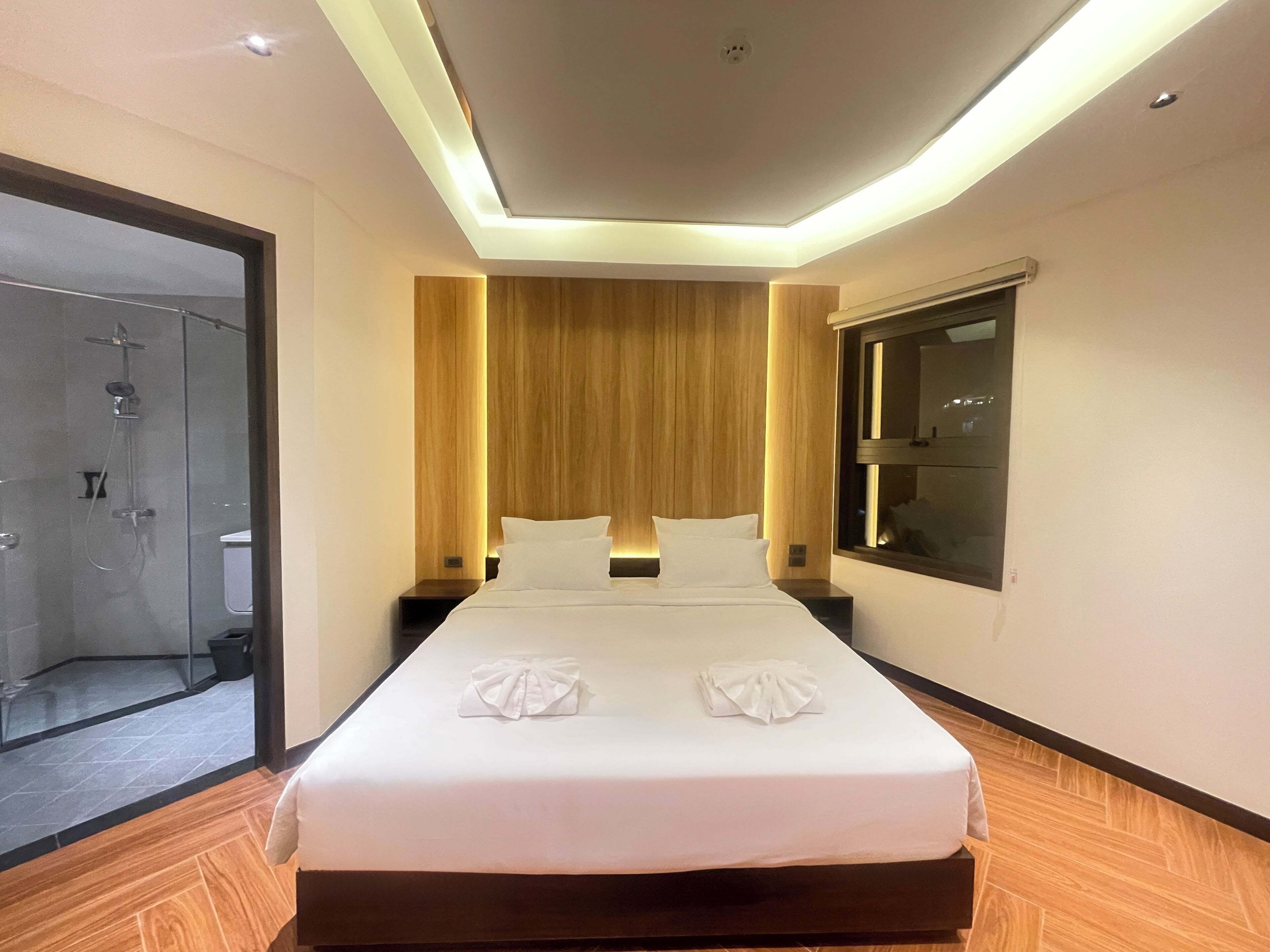 A modern hotel room with a large bed, wooden headboard, and a glass shower enclosure.
