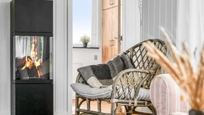Un salon moderne avec une cheminée noire, des meubles en osier et une vue sur l’extérieur.