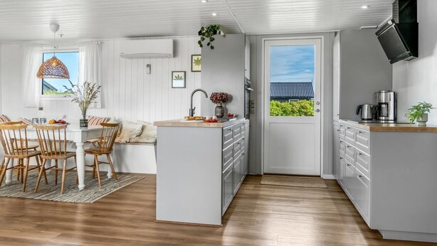 Une cuisine compacte dotée d’un îlot central, d’un coin repas avec des chaises en bois et d’une vue sur l’extérieur, accessible par une porte.