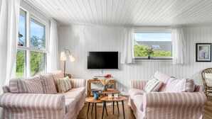 Un salon chaleureux avec deux canapés à rayures, une table basse en bois et un téléviseur à écran plat fixé au mur.