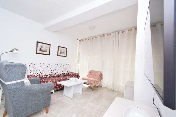 A living room with a sofa, armchair, coffee table, and a flat-screen TV.